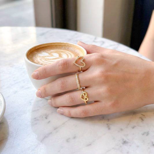 Mujer con café usando anillo corazón circonita, anillo destello y anillo amor infinito dorados enchapados en oro 18K - D'march Designs Chile